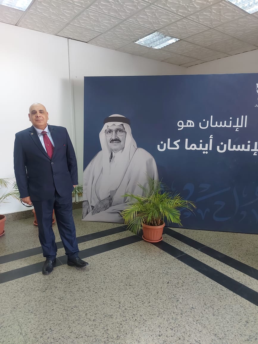 الدكتور إبراهيم شبانة في فعالية ثقافية سعودية أمام لوحة تحمل عبارة الإنسان هو الإنسان أينما كان